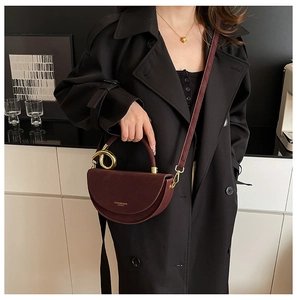 Detail of burgundy half-moon crossbody bag with gold round handle and leather strap