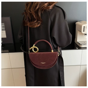 Detail of burgundy semi-circular leather handbag with gold ring handle and logo