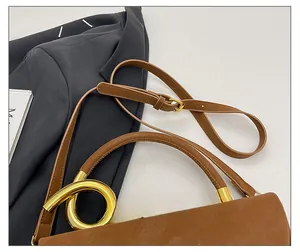 Detail of adjustable leather shoulder strap and golden metal ring on a brown crossbody bag