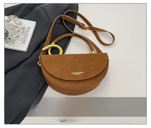 Macro view of caramel leather saddle bag featuring a gold semi-circle metal clasp and strap
