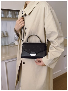 Détail du sac bandoulière noir avec boucle argentée porté sur un trench-coat beige