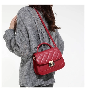 Detail of red quilted handbag featuring a golden turn-lock closure and leather top handle