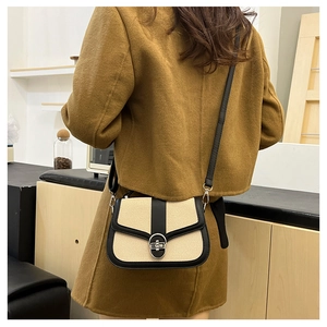Close-up of a stylish contrast crossbody bag with silver oval lock on a brown coat