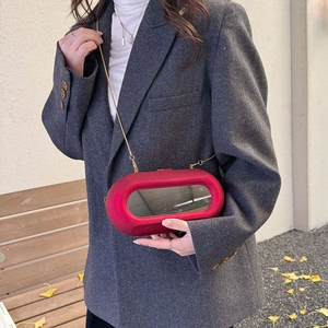 Fashionable red capsule acrylic box bag with gold chain strap on a grey suit model