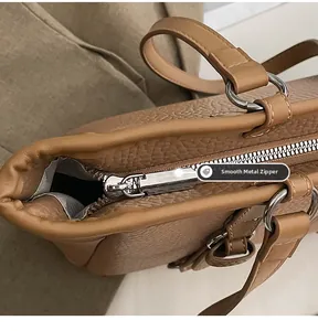 Macro detail of smooth metal zipper and litchi grain texture on brown leather tote bag