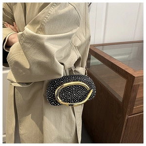 Detail of black rhinestone evening bag with large oval gold metal handle on a coat