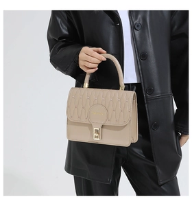 Detail view of beige square handbag with wavy quilting, metal lock, and top handle
