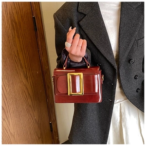 Detail of burgundy leather handbag with a signature oversized gold buckle and hand strap