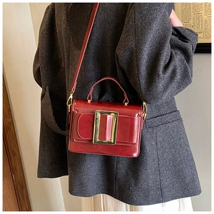 Detail of dark red leather square bag with gold buckle worn over a grey wool coat