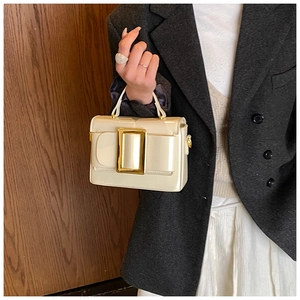 Detail of cream patent leather square handbag with large gold buckle and top handle