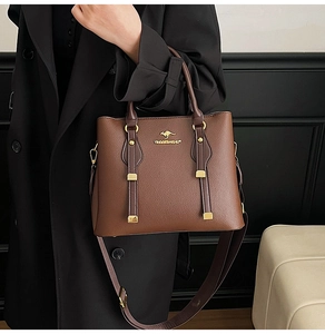 Detail of dark brown pebble leather handbag featuring gold kangaroo logo and sturdy top handles