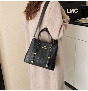 Detail of black woven texture handbag with gold metal logo and sturdy top handle
