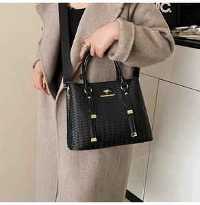 Close-up of black woven texture handbag with golden kangaroo logo and metal zipper detail