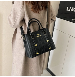 Detailed view of black woven texture handbag with gold kangaroo logo and adjustable strap