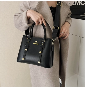 Detail of black pebbled leather tote with golden kangaroo logo and wide nylon shoulder strap