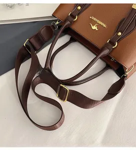 Close-up of adjustable woven shoulder strap and golden kangaroo logo on brown leather bag