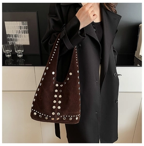 Détail du sac bandoulière en daim marron avec rivets argentés sur un manteau noir