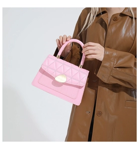 Pink quilted shoulder bag with crocodile texture and golden clasp held by a model