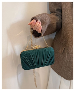 Detail of emerald green pleated satin clutch bag with gold bird clasp and chain strap