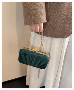 Close-up of pleated dark green satin evening bag with a gold chain and metal clasp