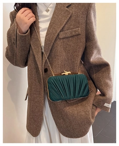 Detailed view of dark green pleated satin evening clutch with gold bird-shaped metal clasp