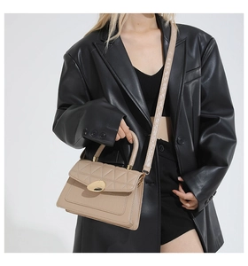 Detail of beige quilted handbag with large gold oval buckle on black leather blazer