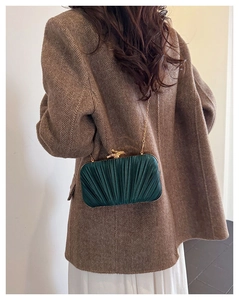 Detail of emerald green pleated evening bag with gold bird clasp worn on suit