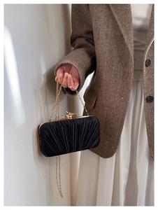 Macro shot of elegant black pleated satin evening bag with decorative gold metal clasp