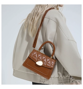 Detail of quilted brown leather handbag with gold metal lock and shoulder strap