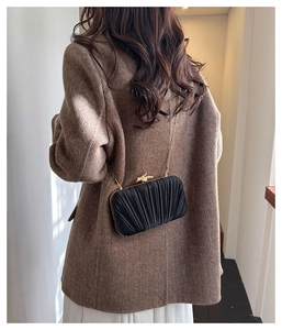 Detail of a black pleated satin evening bag with a gold bird clasp on a wool coat