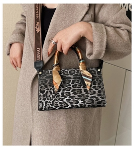 Detail of leopard print handbag featuring silk scarf handle and logo woven strap