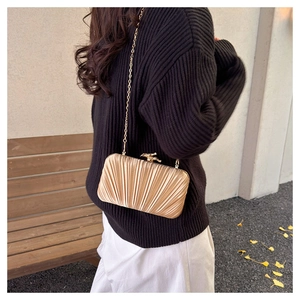 Detail of elegant gold pleated satin evening bag with metal chain on model outfit