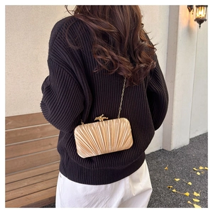 Detail of champagne satin pleated evening bag with elegant bird-shaped metal clasp