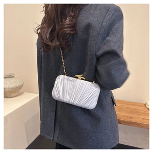 Detail of a satin pleated evening bag with gold bird clasp and chain strap on shoulder