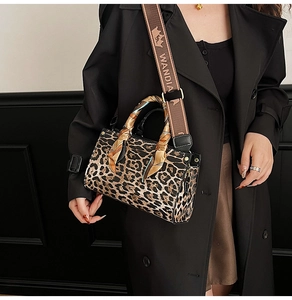 Detail of leopard print handbag with a wide branded strap and decorative silk scarf handle