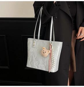 Detail of silver tote bag featuring crinkled metallic texture and plush bear pendant