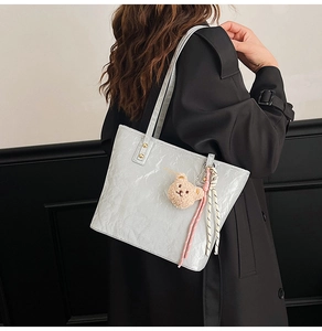 Detail of light gray tote bag with crinkled texture, plush bear charm, and long straps
