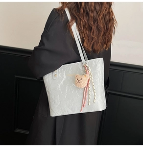 Detail of silver pleated tote bag with plush bear charm shown on a shoulder