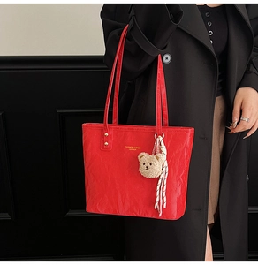Detail of red tote bag with crinkled texture, gold lettering, and a cute bear charm