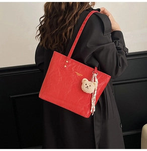 Detail of red glossy leather tote bag with metal rivets and plush bear keychain accessory