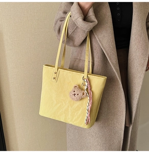 Detail of light yellow tote bag with pleated texture and cute brown bear pendant charm