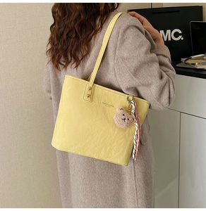 Detail of yellow pleated tote bag with plush bear charm and silk scarf on shoulder