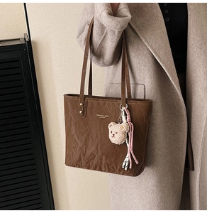 Close-up of brown tote bag with natural texture, logo print and bear charm detail