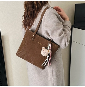 Brown oil wax leather tote bag with fashion lettering and cute bear charm shown on shoulder
