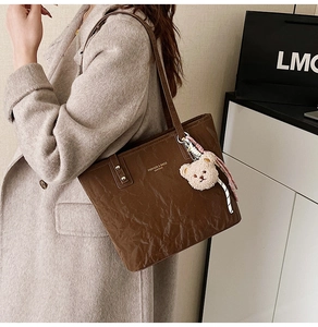 Brown pleated leather tote bag featuring a plush bear charm and fashion logo detail