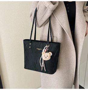 Detail of black leather tote bag featuring gold logo and cute bear charm with pink ribbon