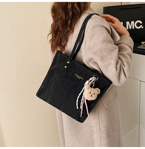 Detail of black leather tote bag with gold lettering, metal studs and plush bear charm