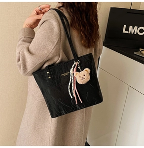 Detail of black tote bag with retro wrinkled texture and plush bear pendant accessory