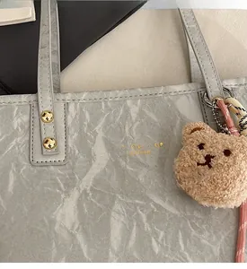 Close-up of grey textured leather tote bag featuring gold lettering and cute bear charm