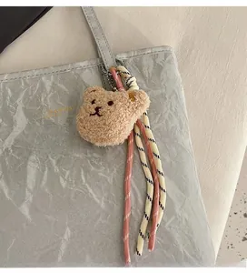 Detail of plush bear bag charm with pink woven rope on a grey leather tote bag